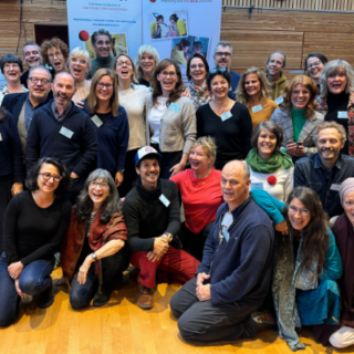 Eine große Gruppe von Menschen posiert lächelnd für ein Gruppenfoto in einem Holzsaal mit Bannern im Hintergrund..