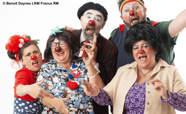 Fünf fröhliche Clowns mit roten Nasen posieren in bunten Kostümen vor weißem Hintergrund und machen lustige Gesichter.