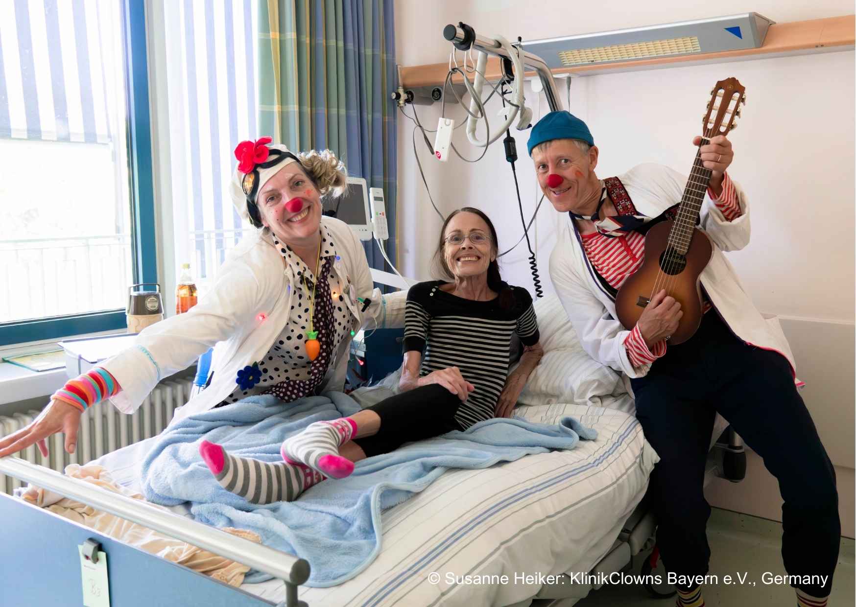 Two clowns next to a patient in a hospital bed